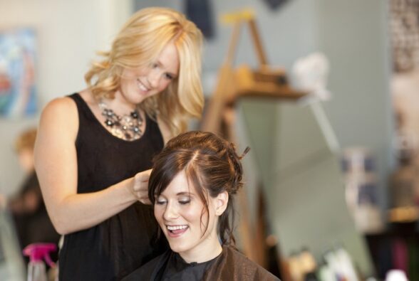 Female adult with blonde hair styling a female adult with brown hair's hair.